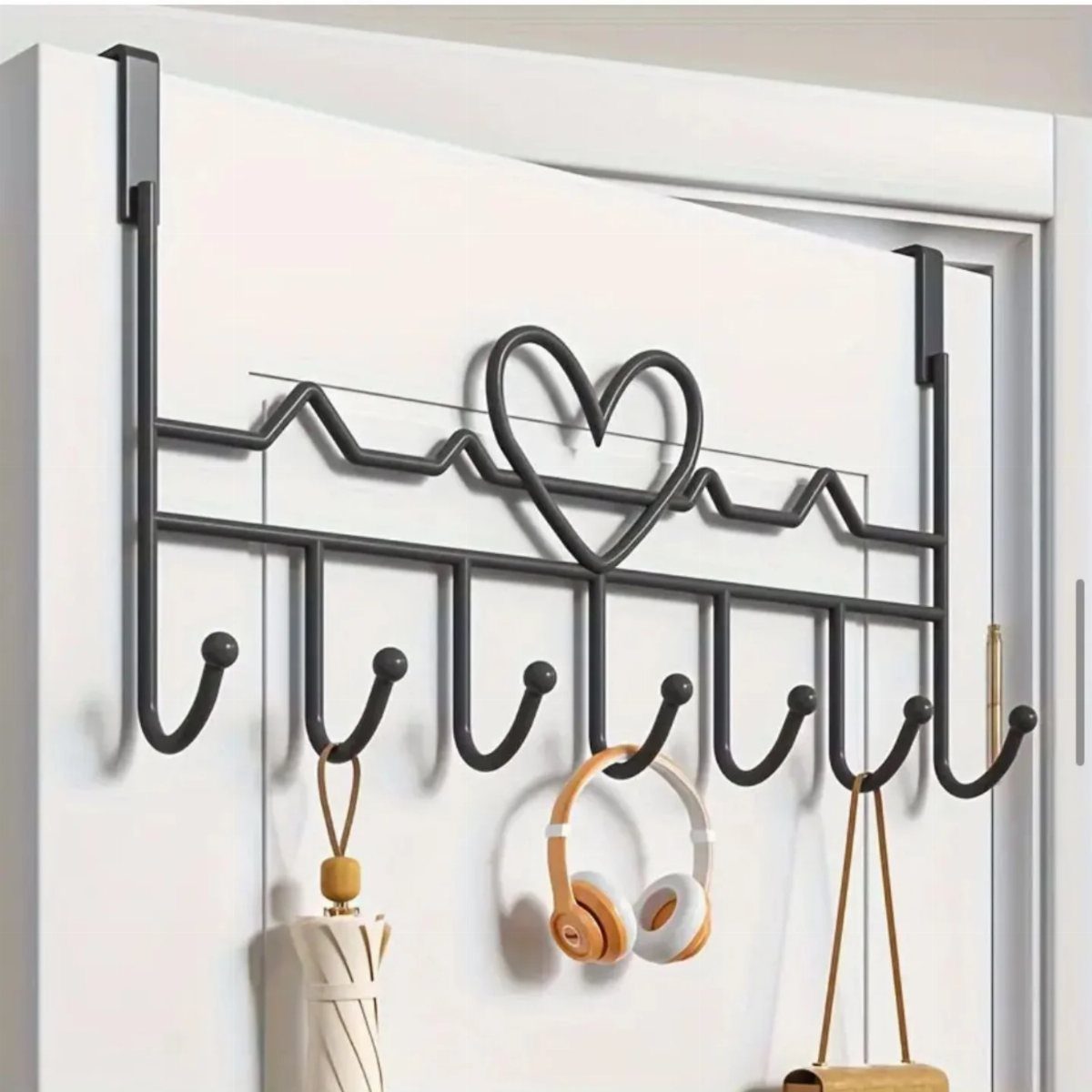 Black metal over-the-door hook rack with heart design holding accessories on white door