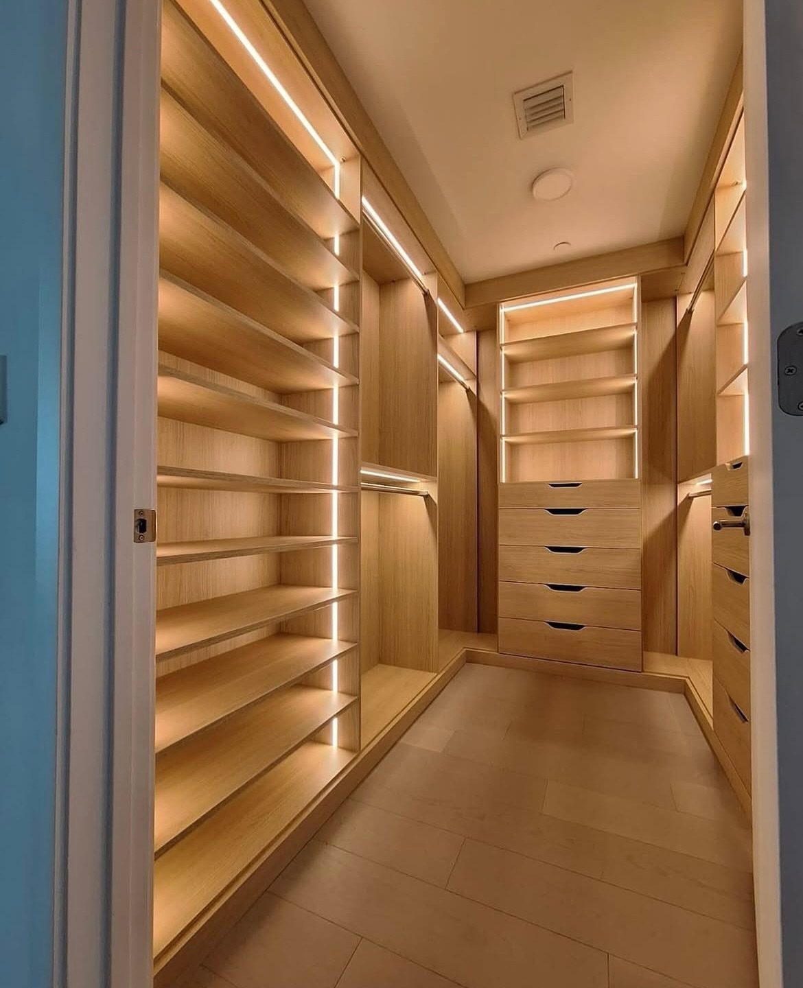 Walk-in open closet with light wood shelving and integrated vertical LED strip lighting