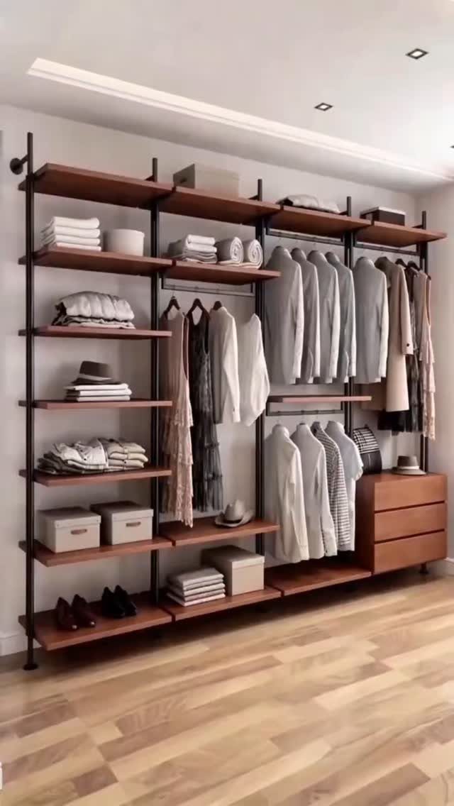 Wall-mounted open closet with wooden shelves and metal pipes holding organized clothing.