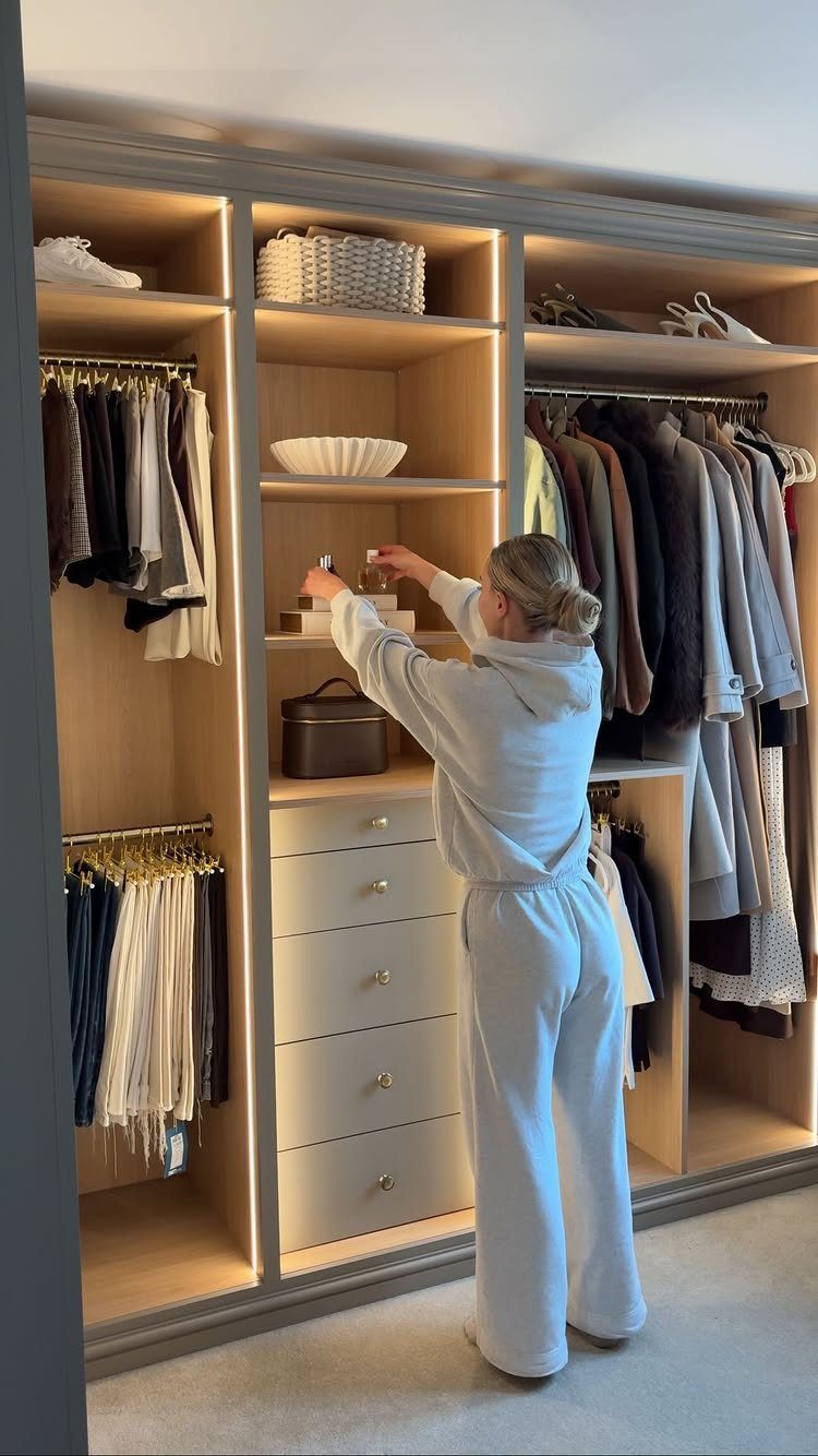 Woman organizing clothes in a modern open closet with built-in lighting and shelving.
