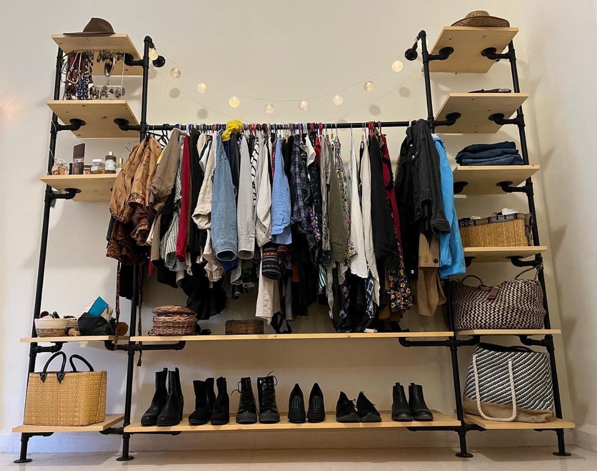 Industrial pipe open wardrobe with wooden shelves, hanging clothes, and shoes.
