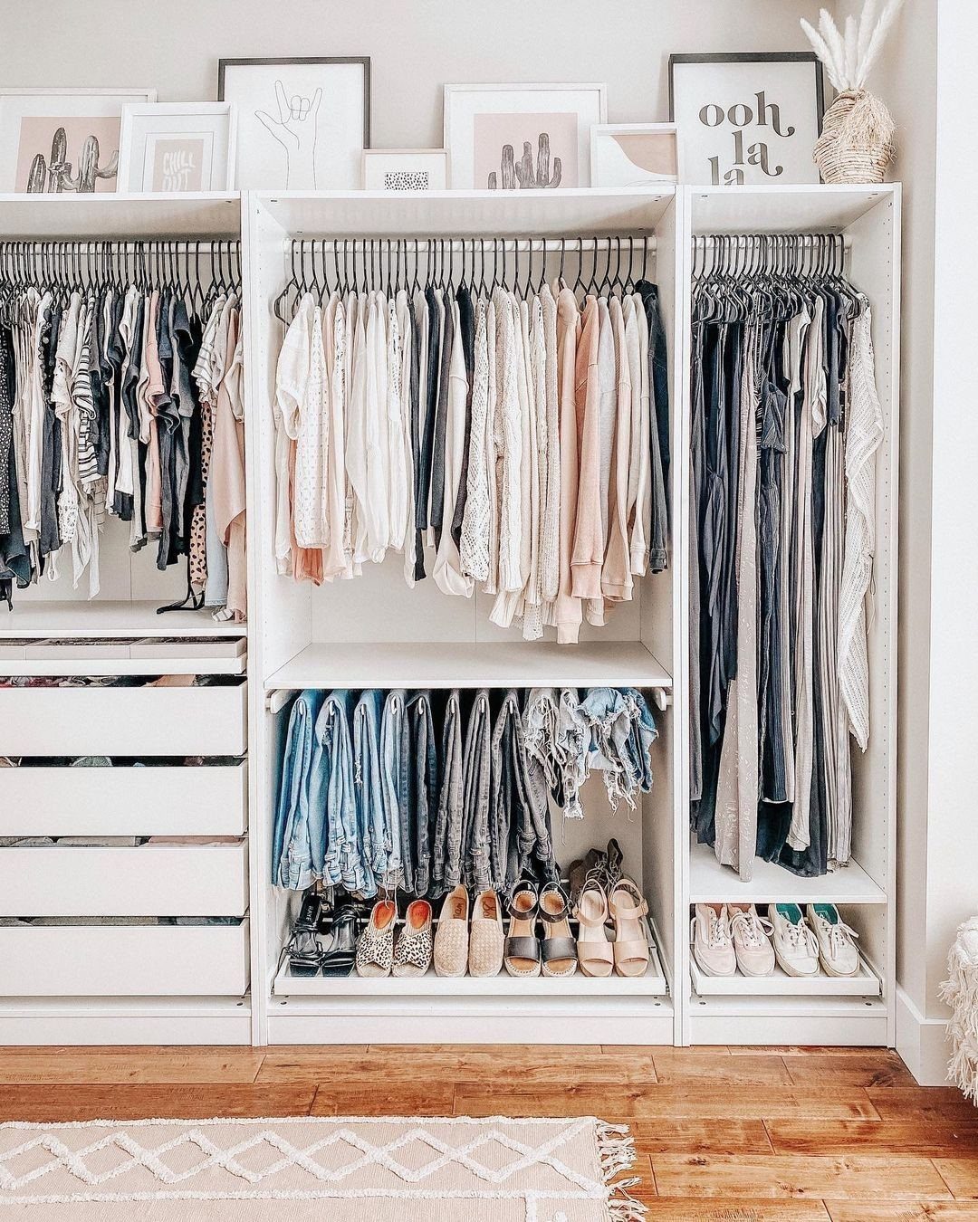 White open closet system with hanging clothes, drawers, and shoes on wooden flooring.