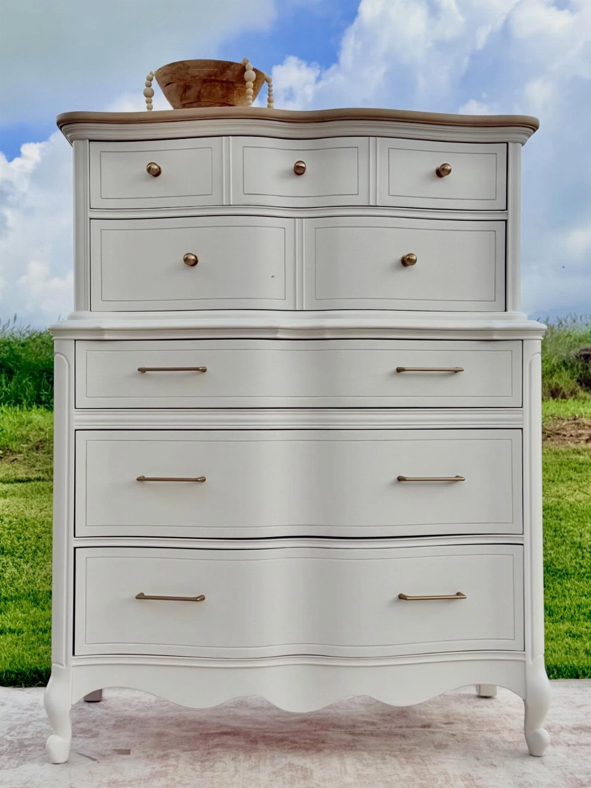 White painted wooden dresser with gold hardware standing outdoors against a cloudy sky.