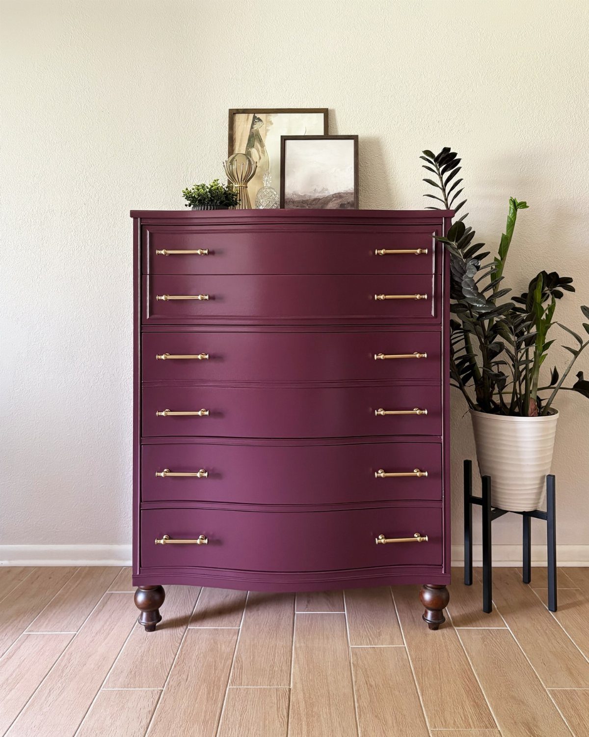 Deep purple painted dresser with gold handles against a cream wall with plants.