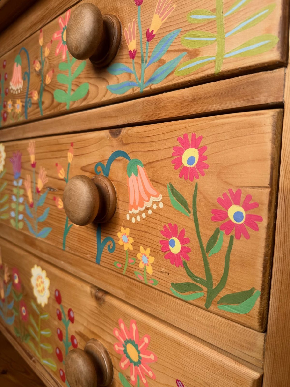 Wooden dresser drawers decorated with colorful hand-painted flowers and green leaves.