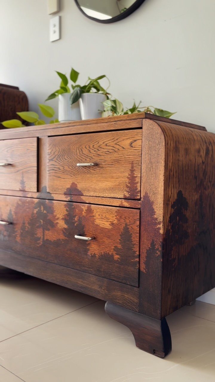 Wooden dresser with a dark brown painted forest landscape on the bottom drawers.