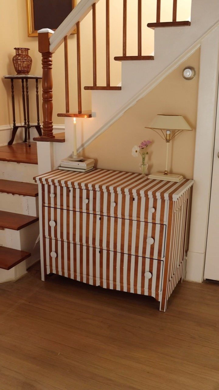 Striped brown and white dresser placed under a wooden staircase in a home.
