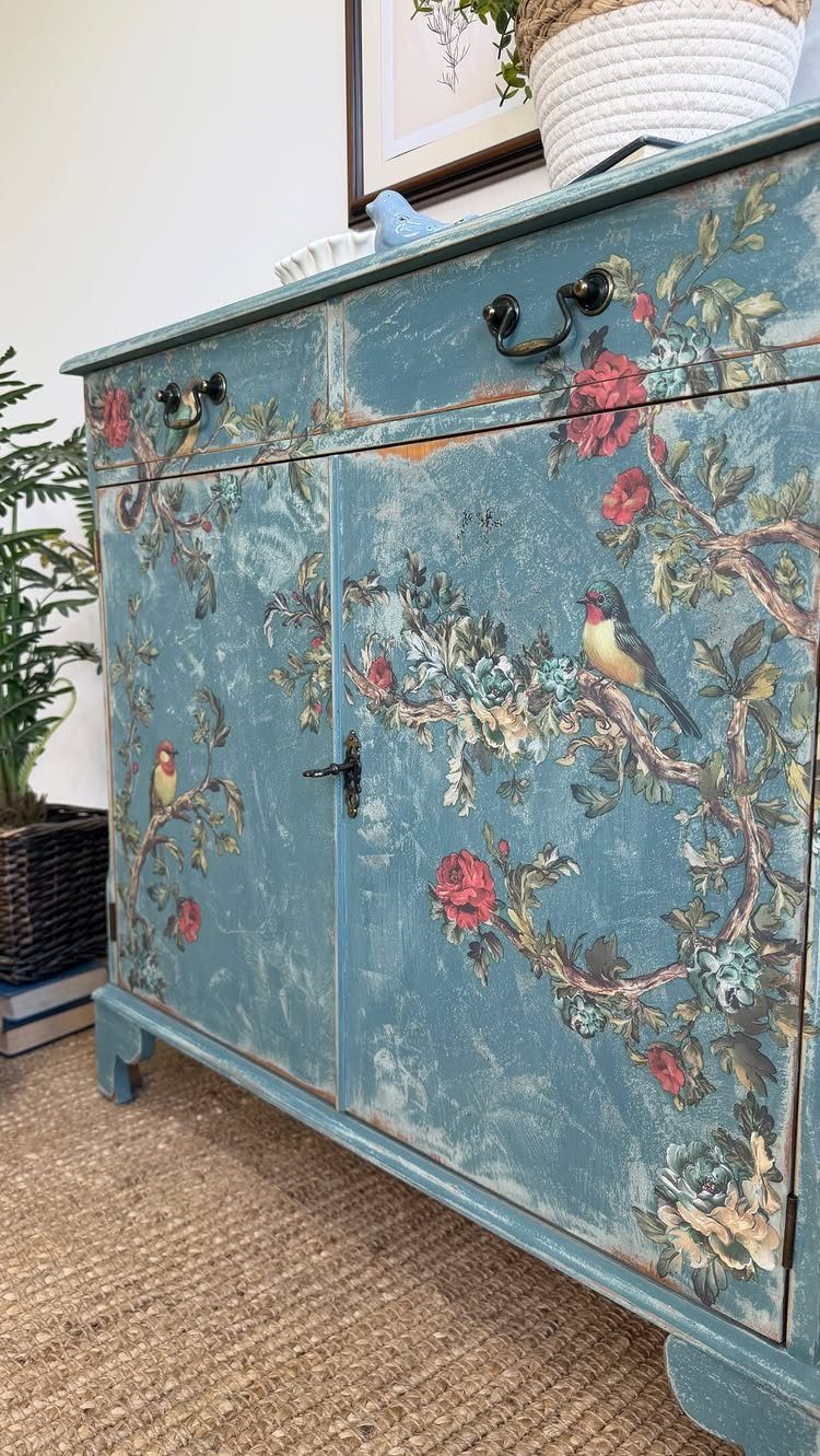 Blue distressed wooden cabinet with painted floral and bird designs on the doors.
