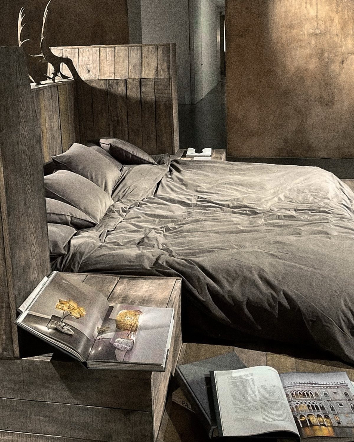 Low bed with grey linens and rustic wooden headboard in minimalist room