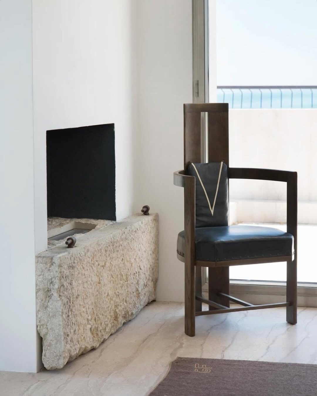 Dark brown wooden armchair with black leather next to a rough stone block.