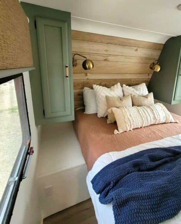RV bedroom with a light wood plank accent wall and green cabinetry.