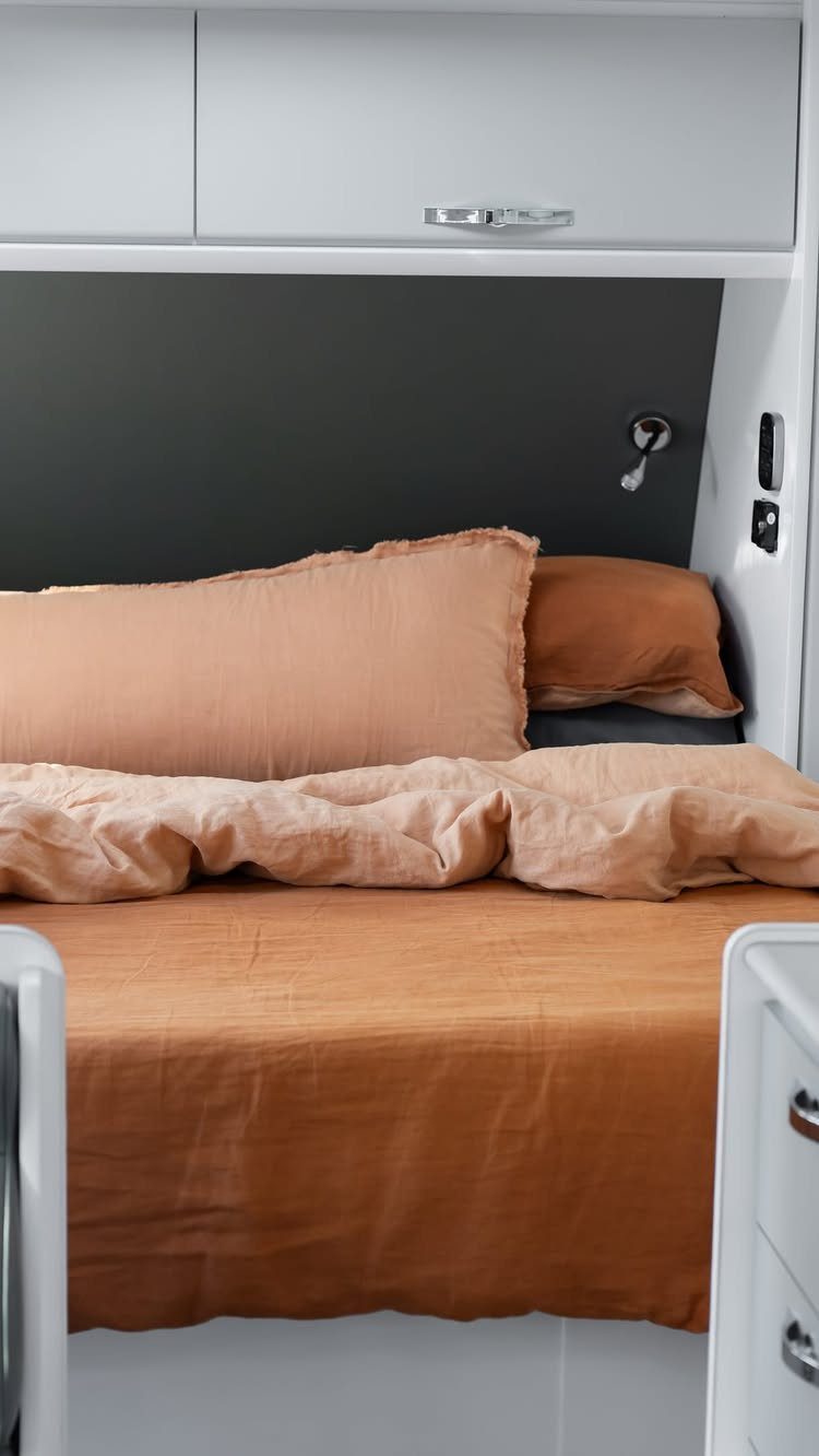 Terracotta linen bedding on a bed inside a modern white and grey RV interior