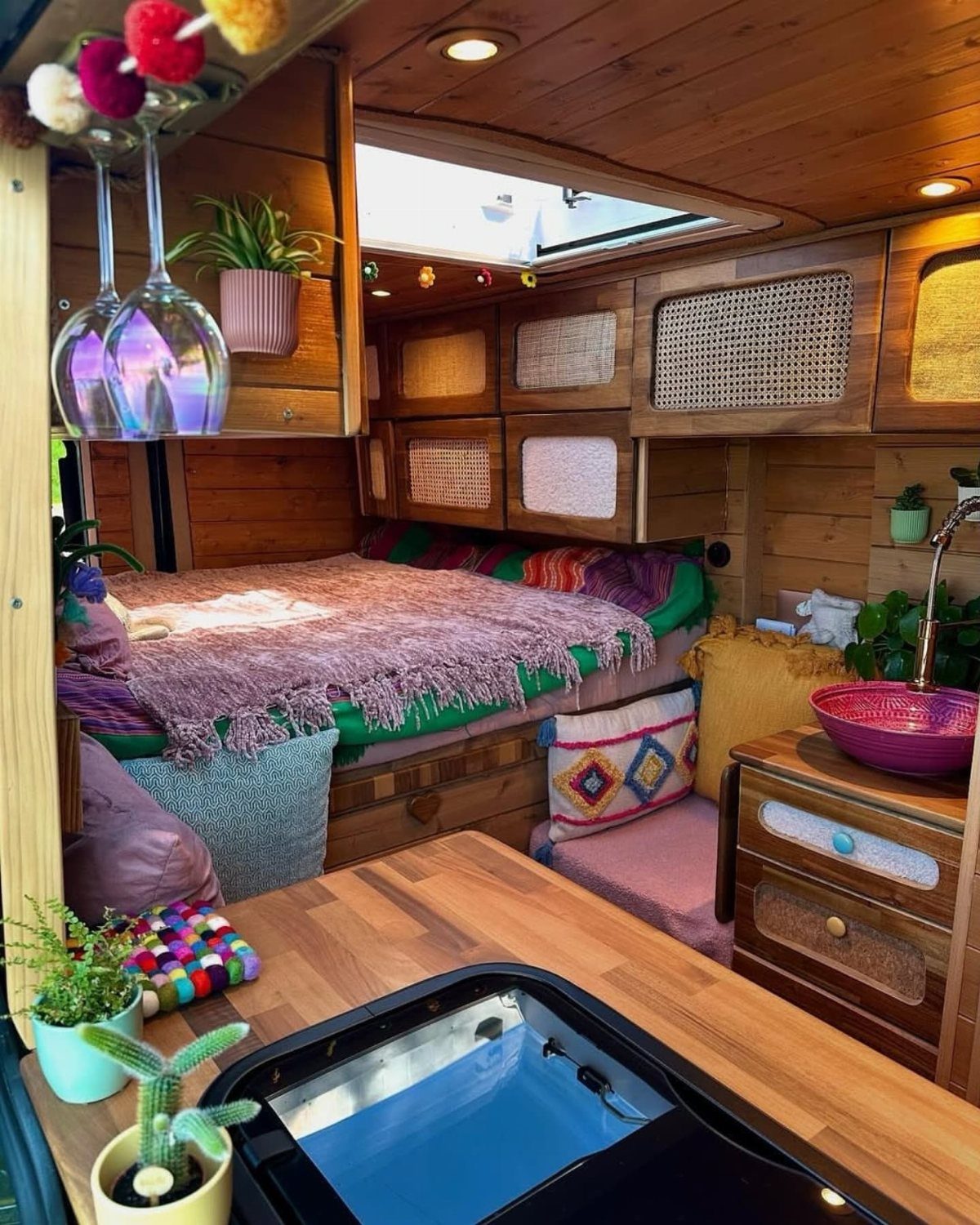 Wooden camper van interior with natural wood walls, ceiling, and a cozy bed.