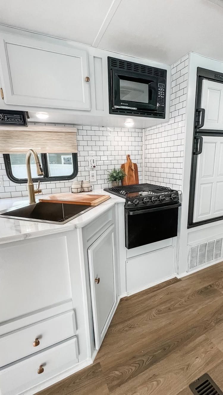 RV kitchen with white subway tile backsplash, white cabinets, and light wood floors.