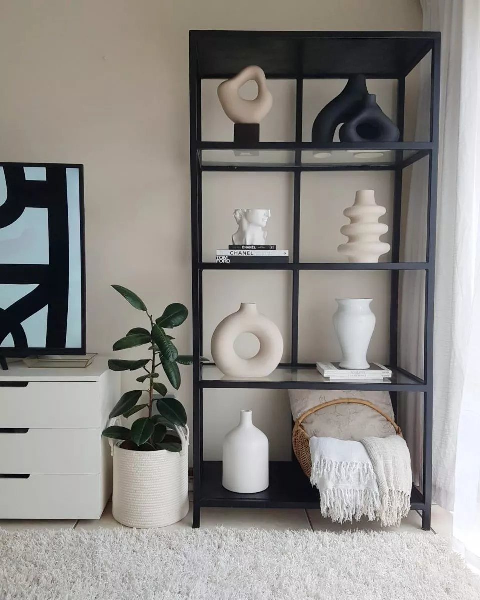 Woven basket with white blanket on the bottom shelf of a black display unit.