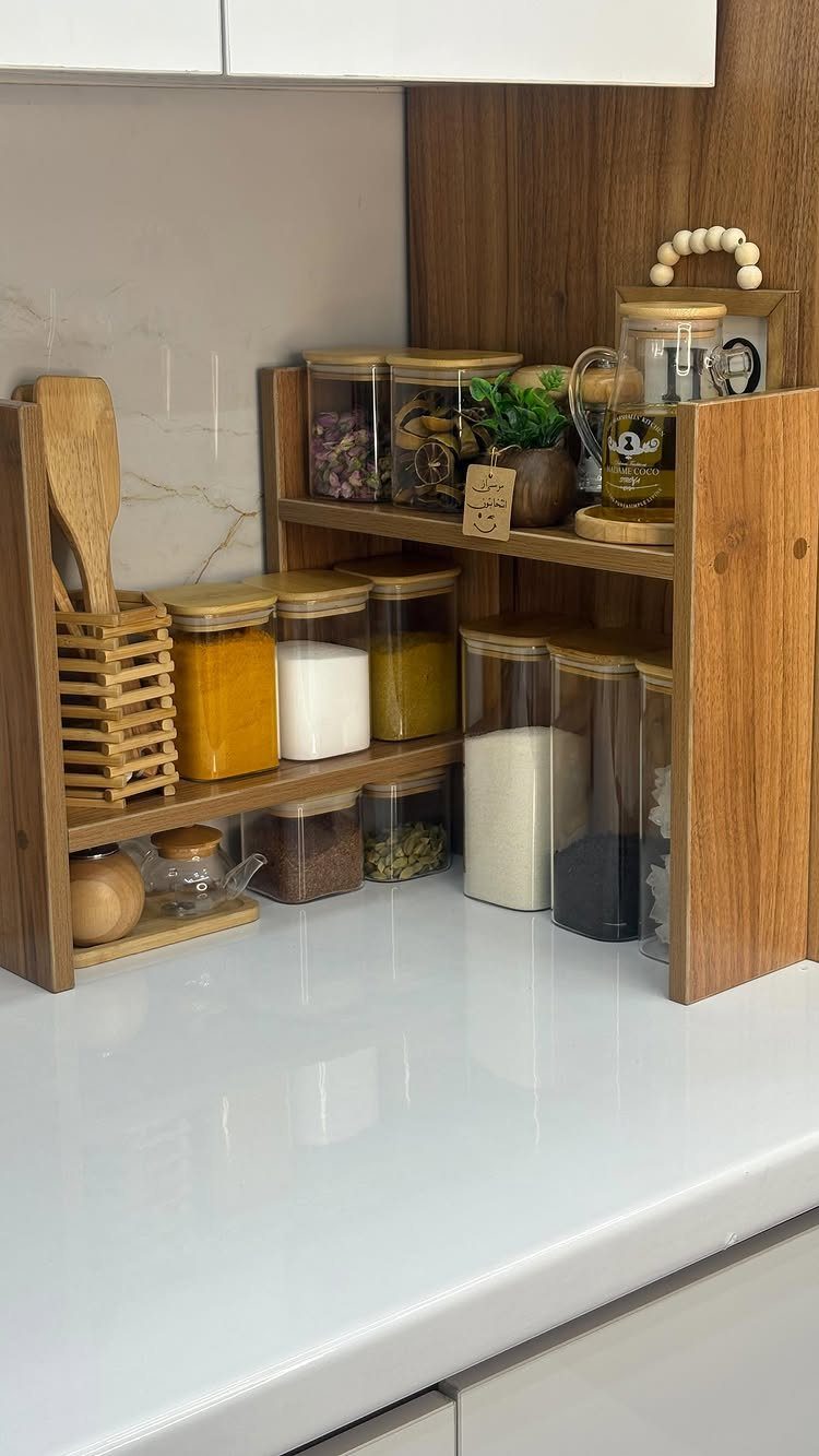 Clear glass jars with wooden lids on a tiered wooden kitchen shelf.