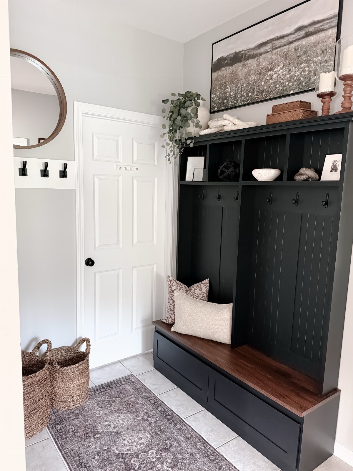 Black hall tree with wooden bench, coat hooks, and cubbies in a bright entryway.