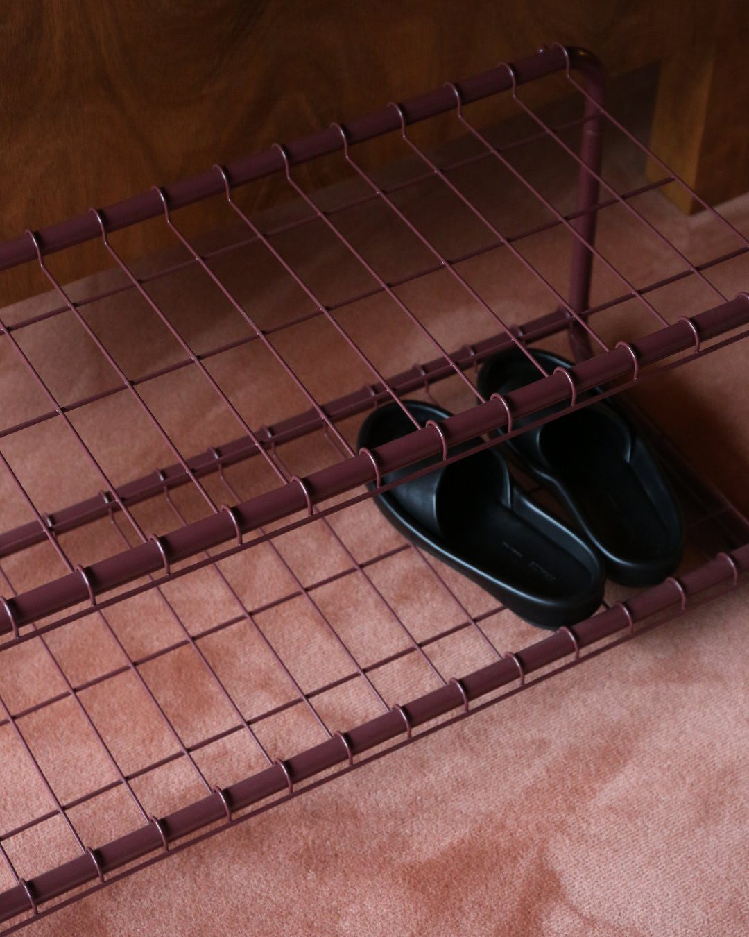 Maroon wire shoe rack with black slip-on shoes on a pinkish floor