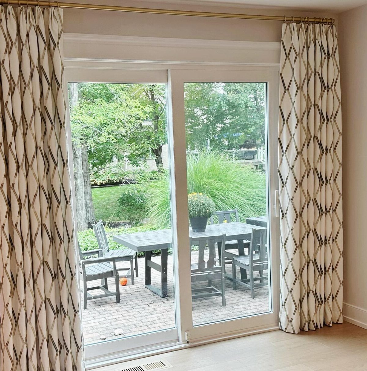 Patterned cream curtains framing a glass sliding door leading to an outdoor patio.