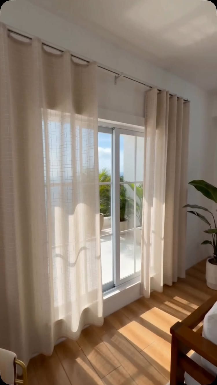 Beige linen curtains hanging over a sliding glass door in a bright room.