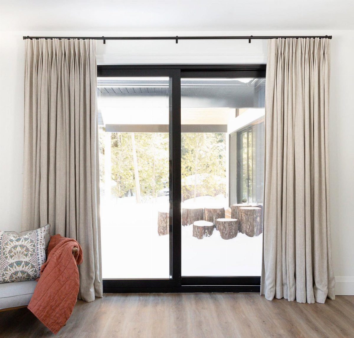 Neutral linen curtain panels framing a black sliding glass door overlooking a snowy yard