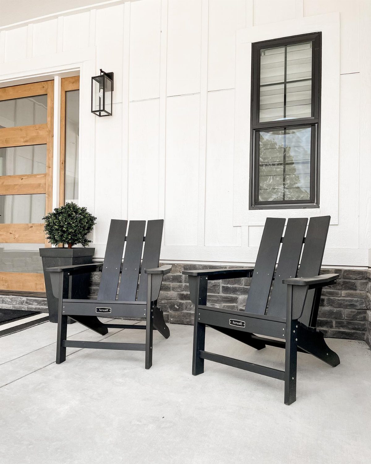 Two black Adirondack chairs on a concrete porch against a white house wall.