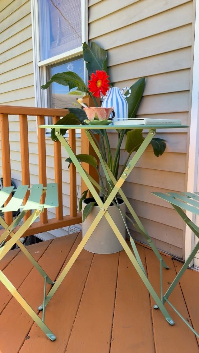 Light green metal bistro set with a small table and chairs on a porch.