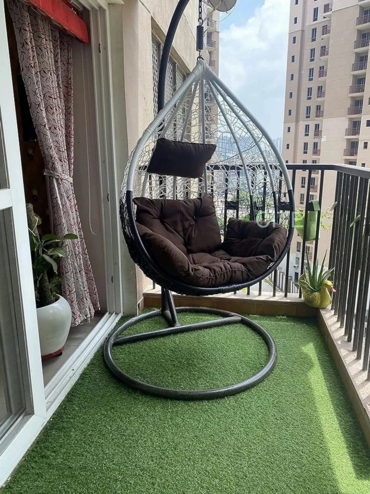 Hanging egg chair with brown cushions on a balcony with artificial grass.