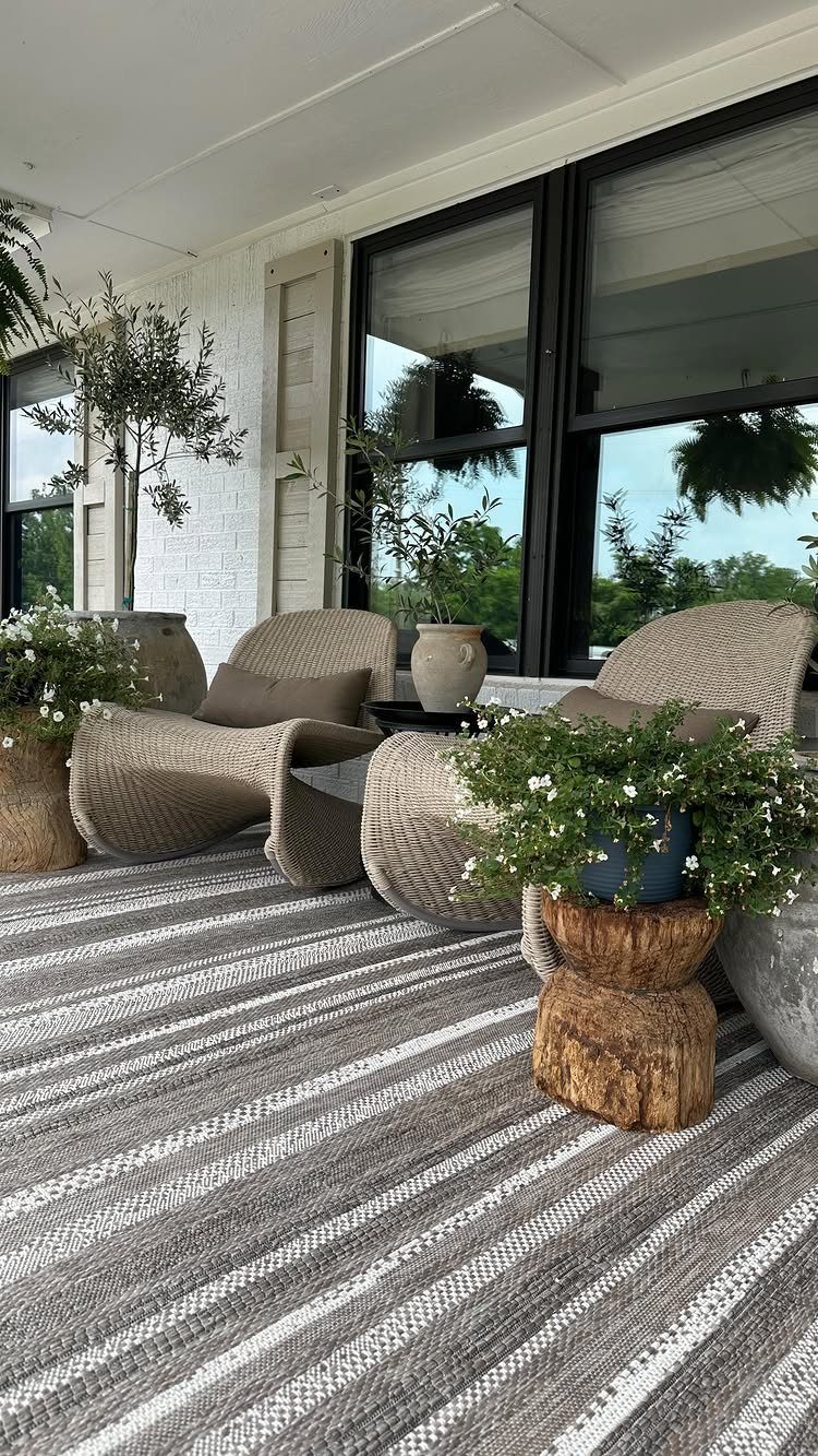 Striped outdoor rug on a porch with woven wicker lounge chairs and plants.