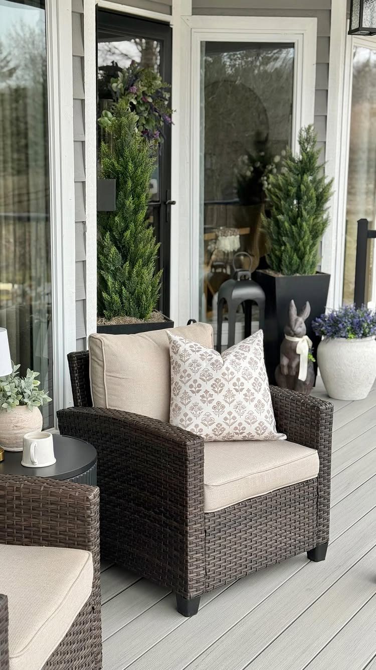 Brown wicker armchairs with beige cushions on a light grey wooden porch.