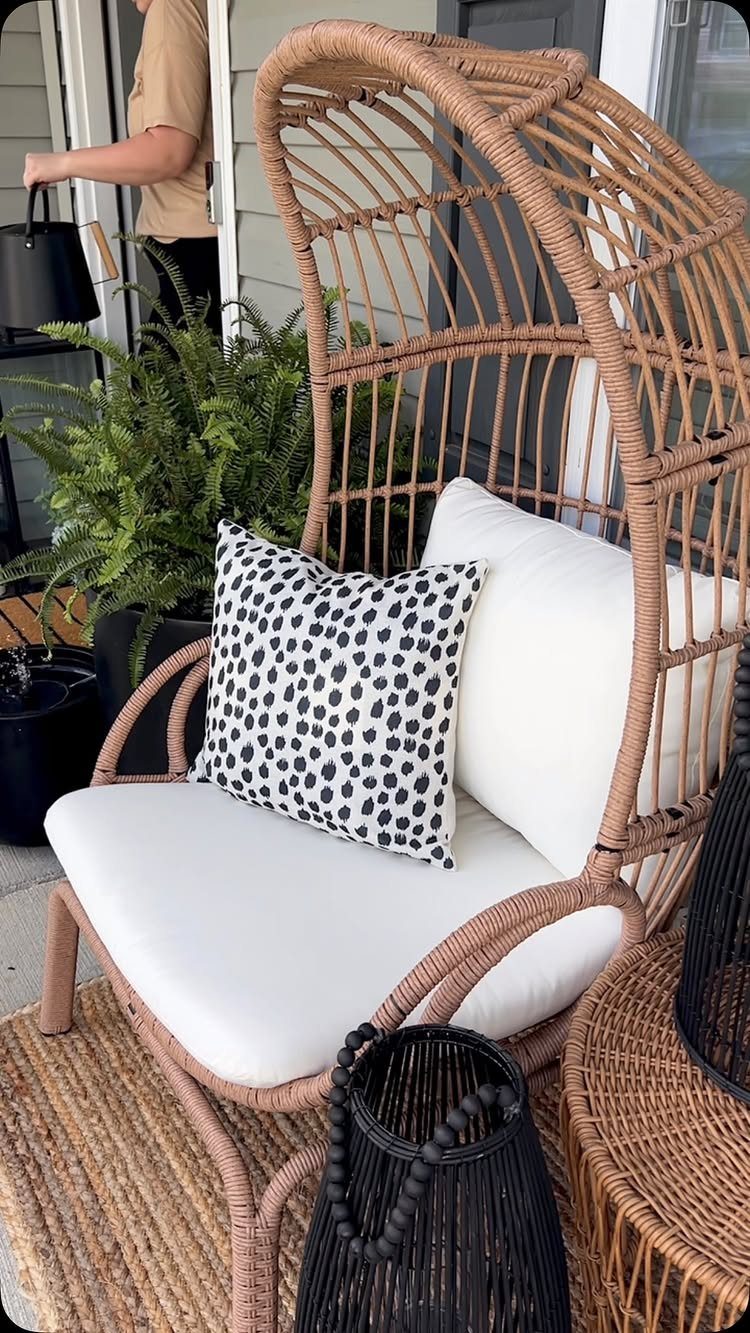 Wicker egg chair with white cushions and spotted pillow on a porch
