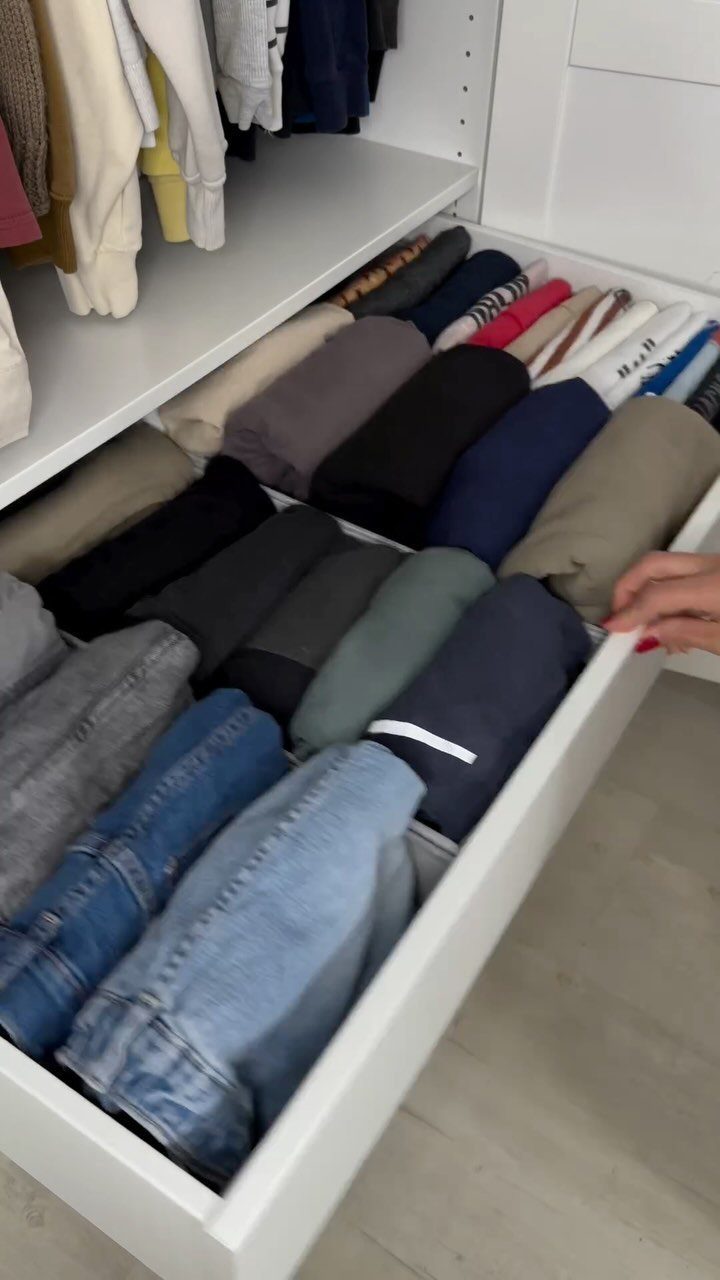 Folded sweaters and jeans organized inside a white open closet drawer.