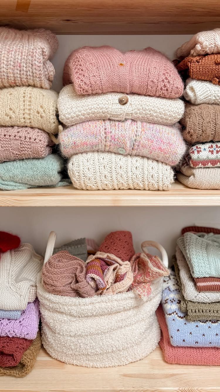 Folded knit sweaters stacked on wooden shelves with a white woven storage basket.