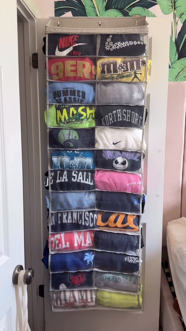 Over-the-door hanging organizer with clear pockets filled with folded colorful sweaters and shirts.