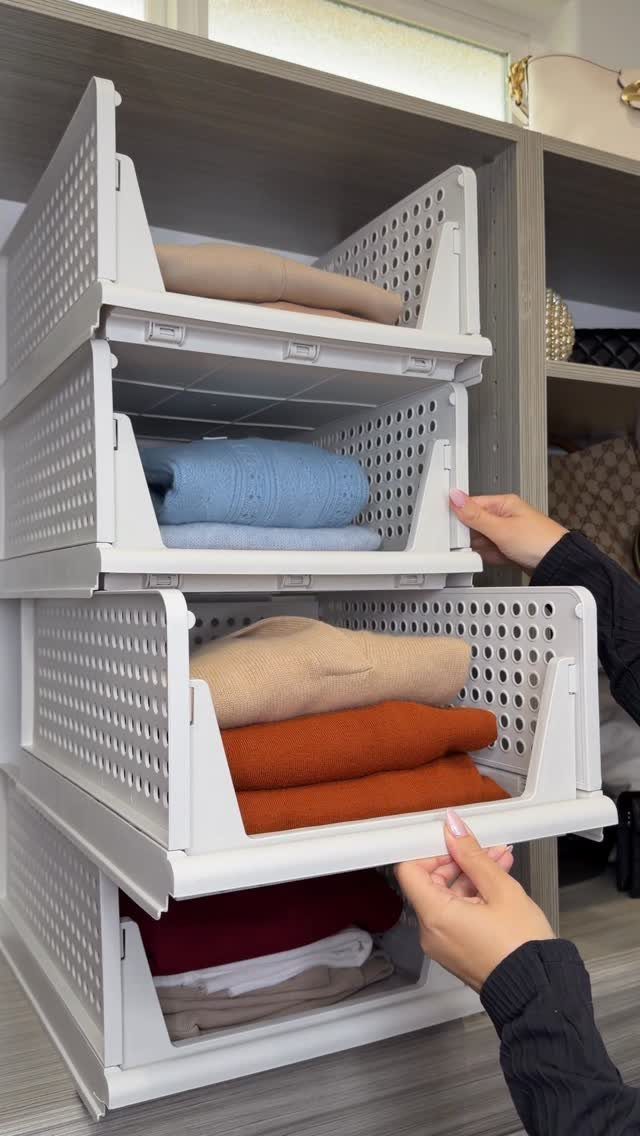 White perforated plastic pull-out bins holding folded sweaters inside a grey shelving unit.