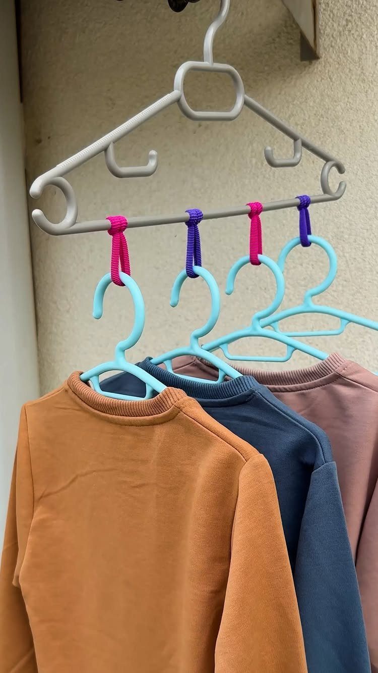 Three sweaters hanging from blue hangers attached to a main white plastic hanger.