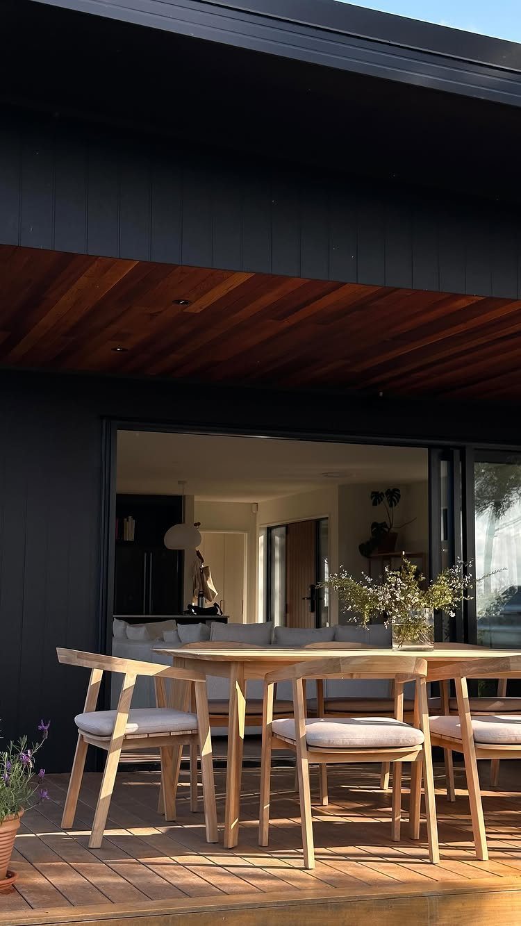 Wooden dining table and chairs with grey cushions on a sunny outdoor deck.