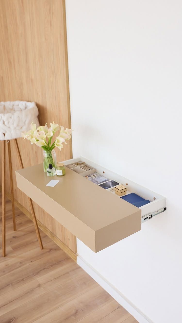 Beige floating wall-mounted desk with open storage and white lilies on top.