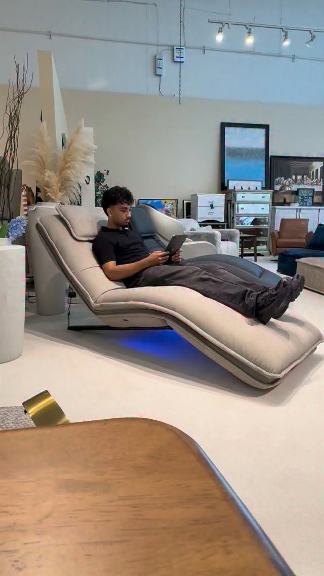 Man reclining in a modern beige ergonomic lounge chair using a tablet in showroom