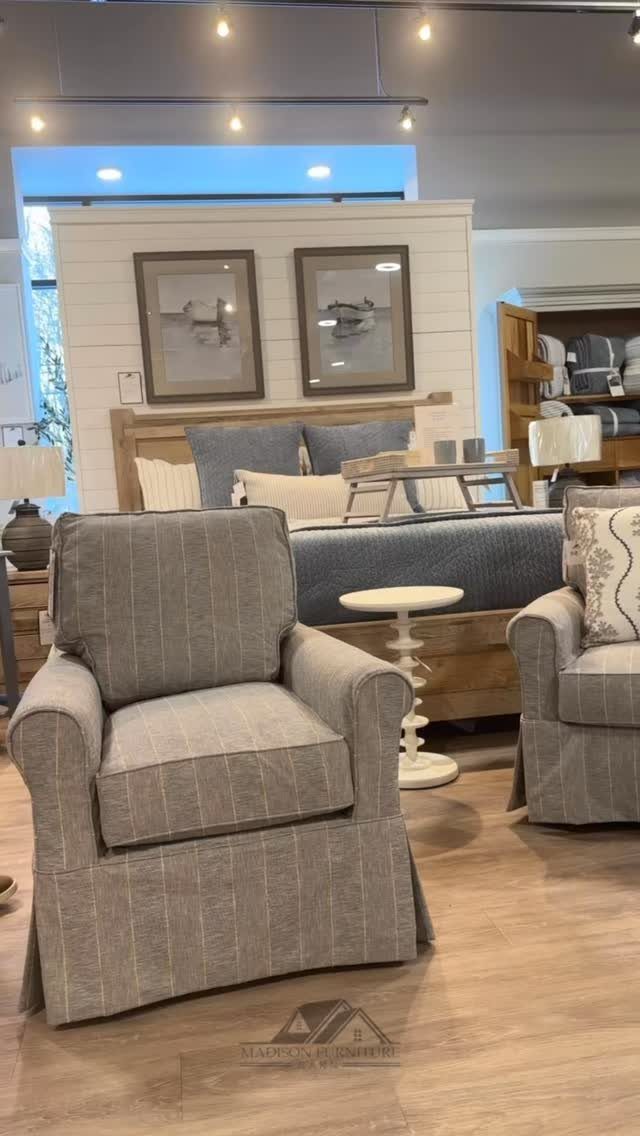 Grey striped slipcovered armchairs in a bright furniture showroom with a bed behind.