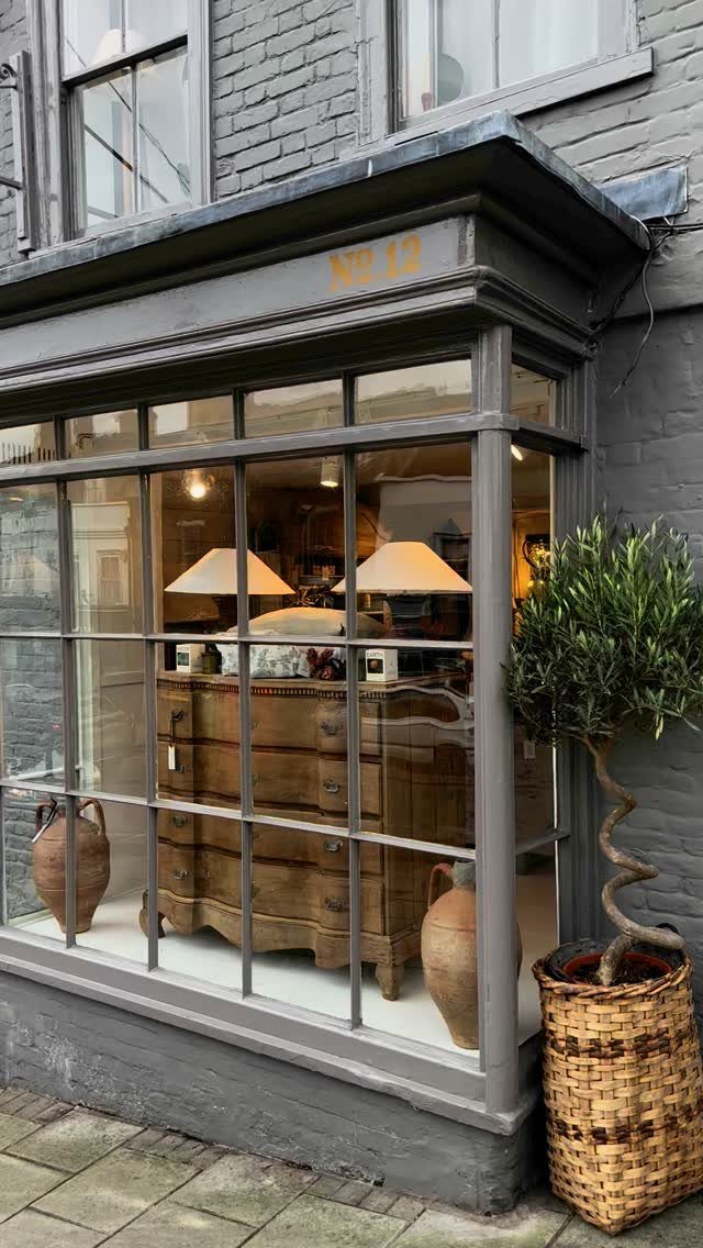 Storefront window displaying a vintage wooden chest of drawers and clay pots.