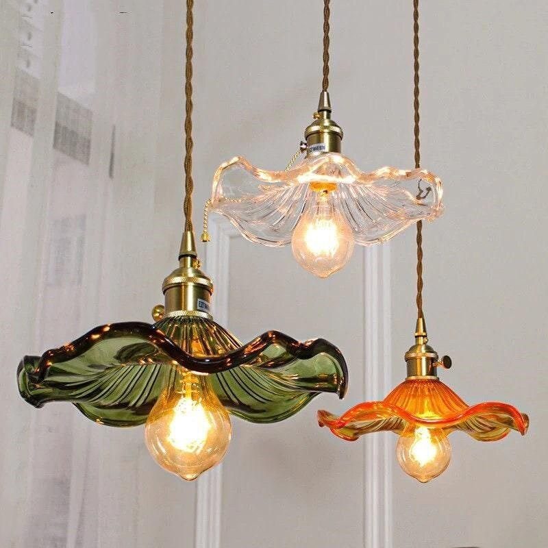 Three flower-shaped glass pendant lights in green, clear, and orange hanging from cords.